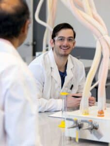 A graduate student wearing a lab coat and safety glasses