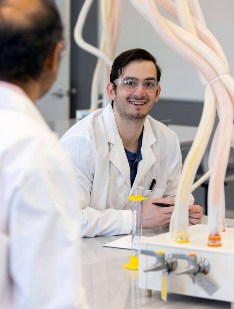 A graduate student wearing a lab coat and safety glasses